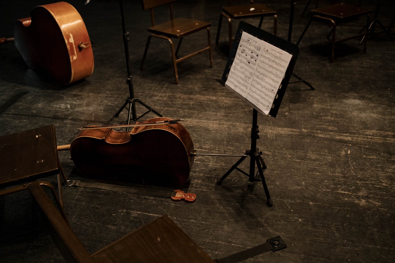 services-06 A cello rests on an empty stage with a music stand and scattered chairs, evoking classical music ambiance.